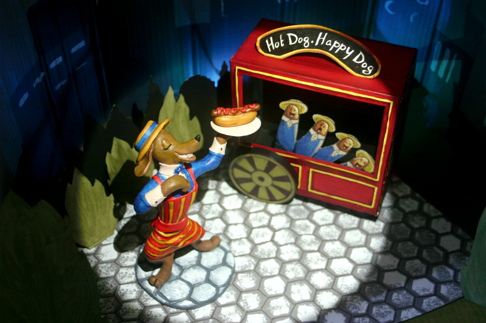 "Hot Dog, Happy Dog" Illustration of Joey, the hotdog vendor, and his happy sausages. 3D model, made with polymer clay, recycled cardboard and acrylic paint.
