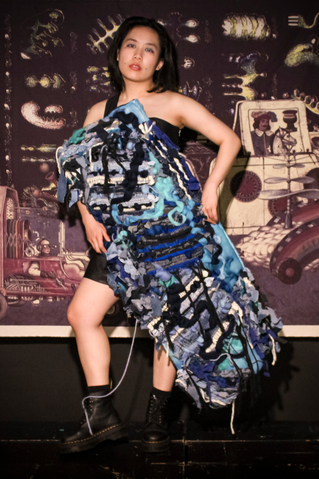 Outfit name: Sorceress Pythia. Moiré dress with wadding panel attached. Wadding panel hand dyed in 3 tones of blue with Saori loom weaving, Peg loom Weaving and Long Arm Quilter wool attachment. The pieces are made from denim from old jeans, wool yarning and merino wool.
