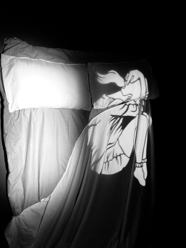 Just passing through. A light projection of a figure on a lonely bed, which you can interact with, but you will stay in different planes of being, her in the light and you in the shadows.
